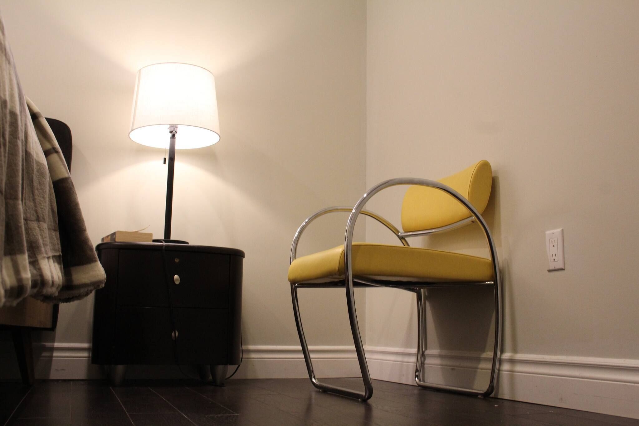 A room with a chair, a lamp, a small table, and a wall socket.
