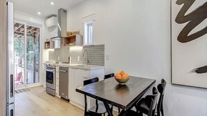 A modern kitchen with a dining table, chairs, and a bowl of fruit.