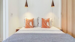 A bedroom with a bed, two bedside tables, two hanging pendant lights, and a wardrobe.