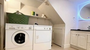A laundry room with a front-loading washer and dryer, a green basket, and a tiled floor.