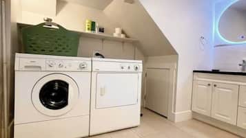 Een wasserette met een voorlader wasmachine en droger, een groene mand en een betegelde vloer.