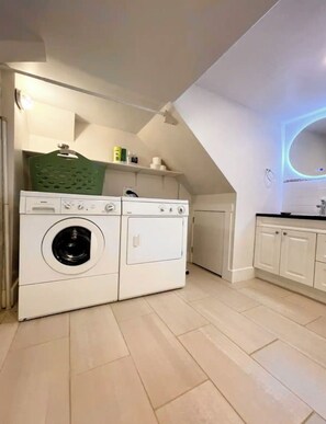 A laundry room with a front-loading washer and dryer, a green basket, and a tiled floor.