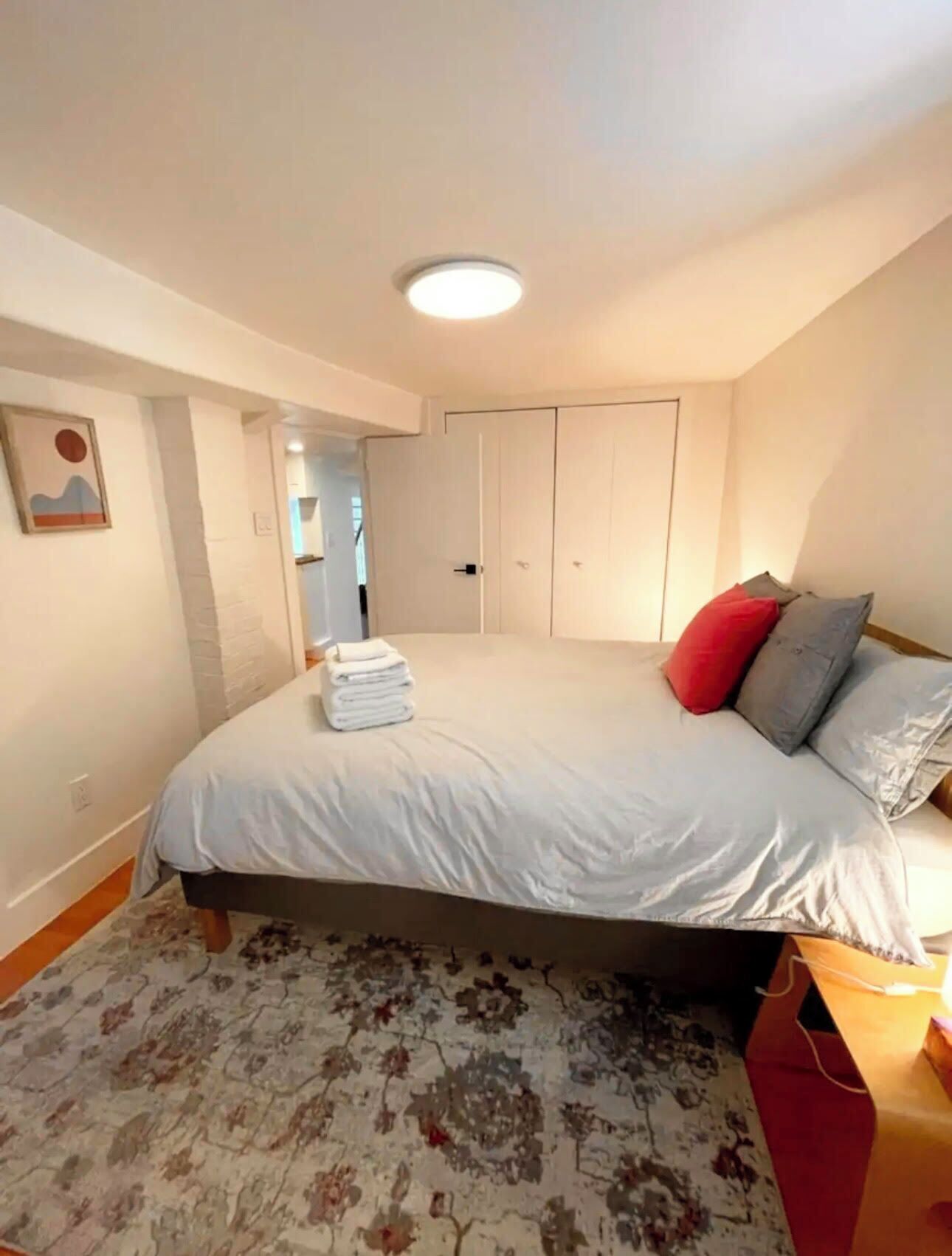 Un dormitorio con cama, armario, mesita de noche y una bolsa roja.