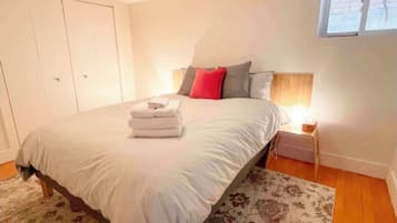 Quarto com cama, mesa de cabeceira, janela e guarda-roupa.