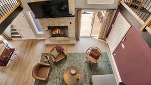 Een ruime woonkamer met een open haard, een bank, een fauteuil en een salontafel.