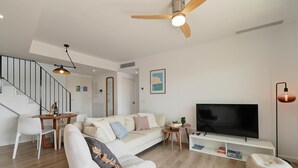 Ein modernes Wohnzimmer mit Sofa, Fernseher, Deckenventilator und Treppe.