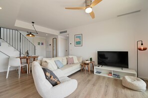 A modern living room with a sofa, a TV, a ceiling fan, and a staircase. - Altos Javea - Javea, Costa Blanca (Javea)