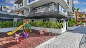 Ein modernes Wohngebäude mit mehreren Balkonen, einem Spielplatz für Kinder und einem gepflasterten Weg.
