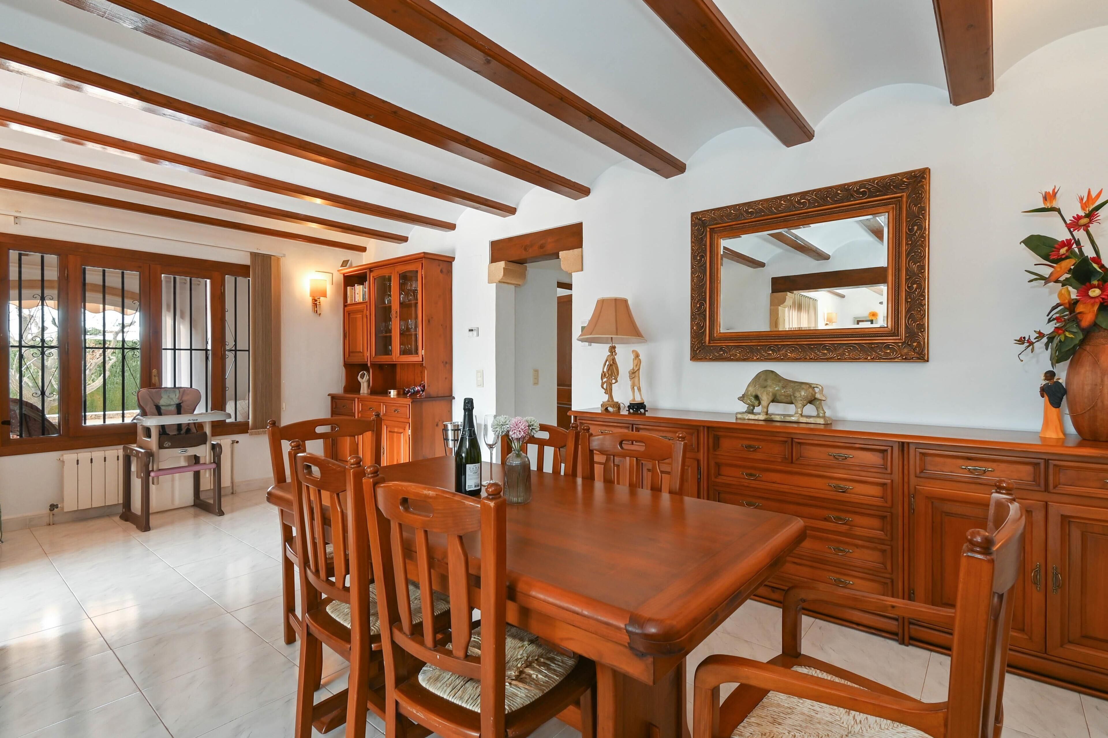A dining area with wooden furniture, a large mirror, and a view of the outdoors through large windows.