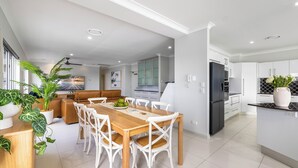 A modern kitchen with white cabinets, a black refrigerator, and a dining area with a wooden table and white chairs. - Admiralty Cove (Sunshine Coast)