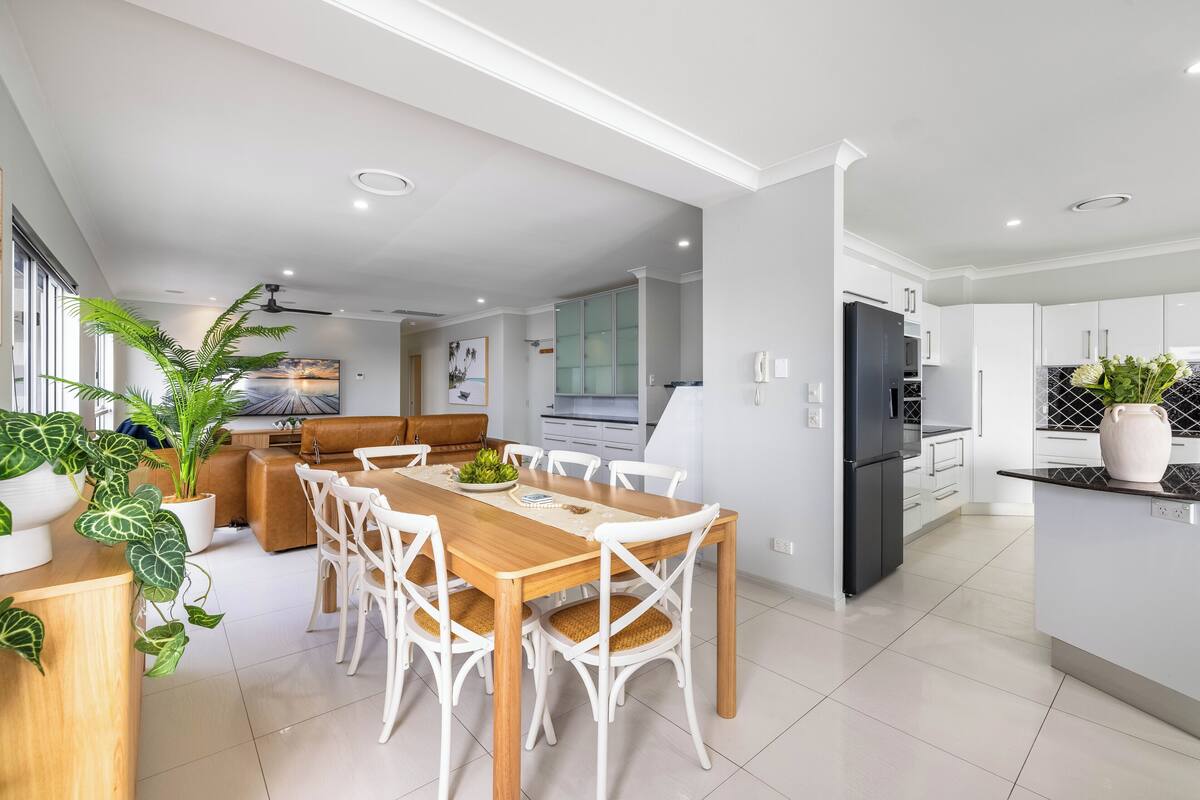 Une cuisine moderne avec des meubles blancs, un réfrigérateur noir et un coin repas comprenant une table en bois et des chaises blanches.