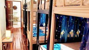 Une chambre avec un lit superposé, un ventilateur de plafond, une petite table de chevet avec une lampe et un rideau décoré sur le thème du ciel étoilé.