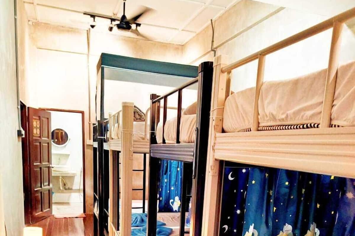 Ein Schlafzimmer mit Etagenbetten, einem Deckenventilator, einem kleinen Nachttisch mit Lampe und einem Vorhang mit Sternenhimmel-Motiv.