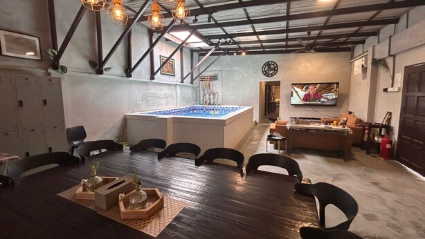 Une pièce spacieuse avec une grande table en bois, plusieurs chaises, une petite piscine et un téléviseur.