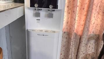 A Cuckoo water dispenser in a kitchen with a patterned curtain in the background.