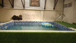 Une piscine intérieure avec un bord carrelé à motifs, un escalier d’accès à la piscine et un élément décoratif en forme d’engrenage fixé au mur.