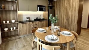 A modern kitchen with wooden cabinets, a dining table with chairs, and a microwave. - Torre Margot (Guadalajara)