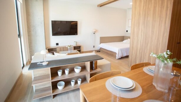 A modern hotel room with a wooden dining table, a sofa, a TV mounted on the wall, and a bed with a wooden headboard. - Torre Margot (Guadalajara)