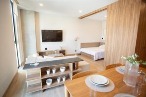 Ein modernes Hotelzimmer mit Esstisch aus Holz, einer Couch, einem an der Wand montierten Fernseher und einem Bett mit Holz Kopfteil.