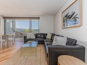 Ett modernt vardagsrum med en hörnsoffa, ett soffbord i glas och en matplats med vita stolar.