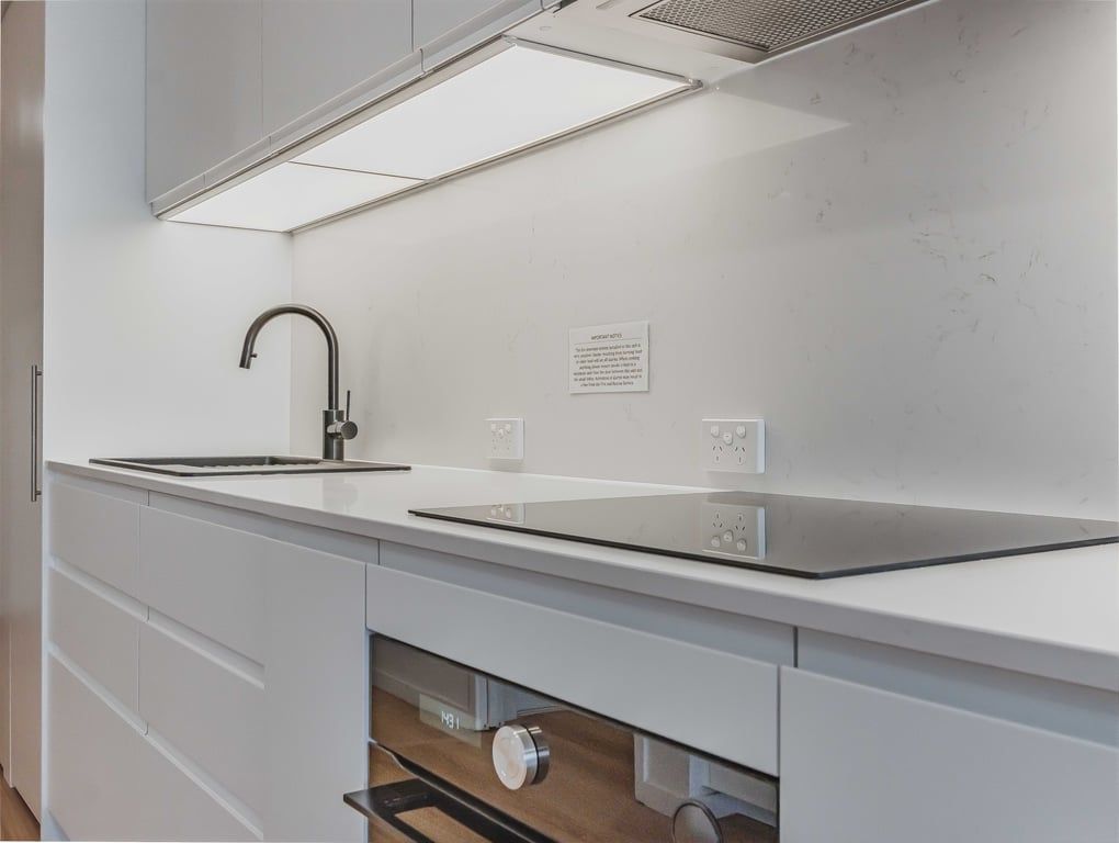 Une cuisine moderne dotée d’un robinet noir élégant, de meubles blancs et d’un four encastré.