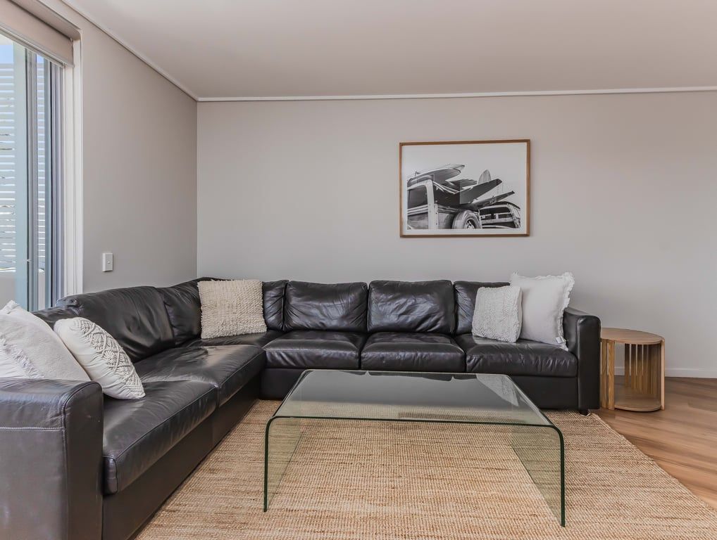 Un salon moderne avec un canapé d’angle en cuir, une table basse en verre et un tableau encadré au mur.