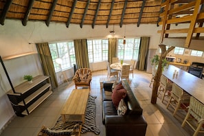 A spacious living area with a thatched roof, a dining table, a sofa, and a bar area with wicker chairs. - Sable Ranch Selfsorg (Brits)