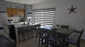 Moderni keittiö, jossa on keskeinen keittiösaareke, baarituolit, ruokapöytä tuoleineen sekä seinällä koristeellinen tähtikuvio.