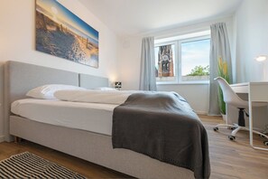 A modern hotel room with a bed, a desk, and a view of a building through the window. - Captain’s Nest: Stylish, near harbour, 2 parking spaces (Bremerhaven)