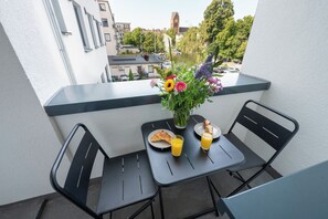 A balcony with a table set for two, featuring a vase of flowers, plates with food, and glasses of orange juice. - Captain’s Nest: Stylish, near harbour, 2 parking spaces (Bremerhaven)