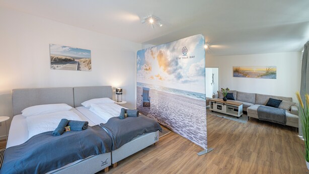 Ett hotellrum med en säng, en soffa, ett soffbord och en bakgrund som är dekorerad i strandtema.