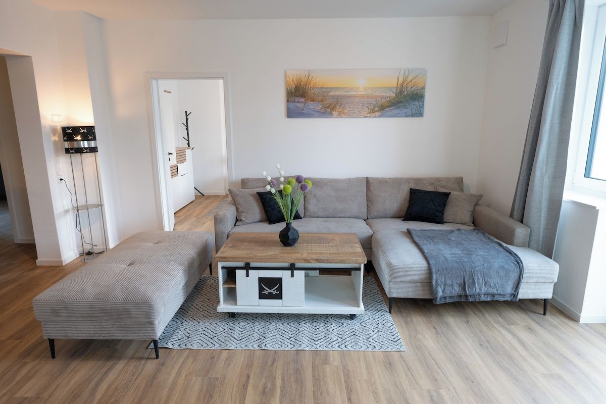 A modern living room with a sofa, a coffee table, and a bench. There is a painting on the wall and a lamp on the left.