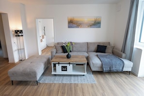 Ein modernes Wohnzimmer mit einer Couch, einem Couchtisch und einer Bank. An der Wand hängt ein Gemälde und links steht eine Lampe.