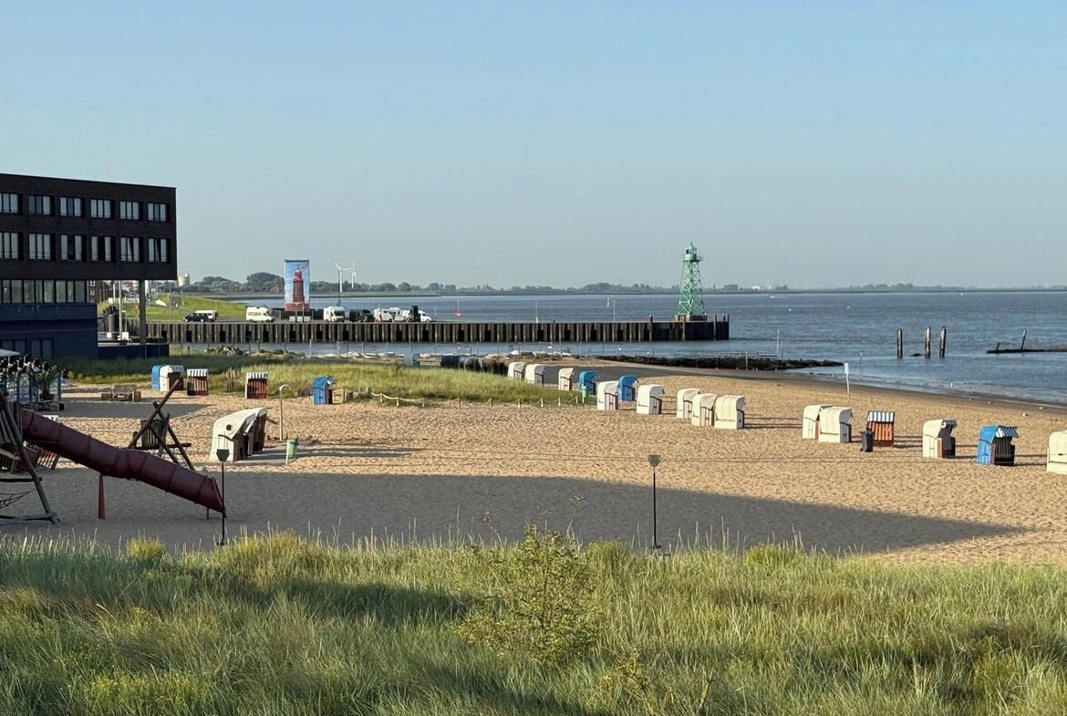 A beach with portable toilets, a pier, and a building in the background.