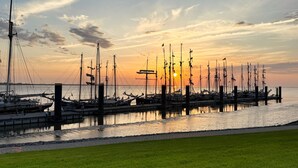 En småbåtshamn med flera båtar förtöjda, en gräsyta i förgrunden och en solnedgång i bakgrunden.