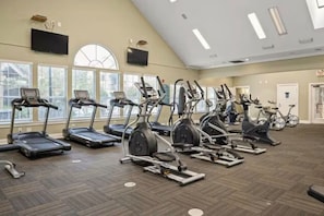 Un gimnasio con cintas de correr, elípticas y bicicletas estáticas dispuestas en filas.