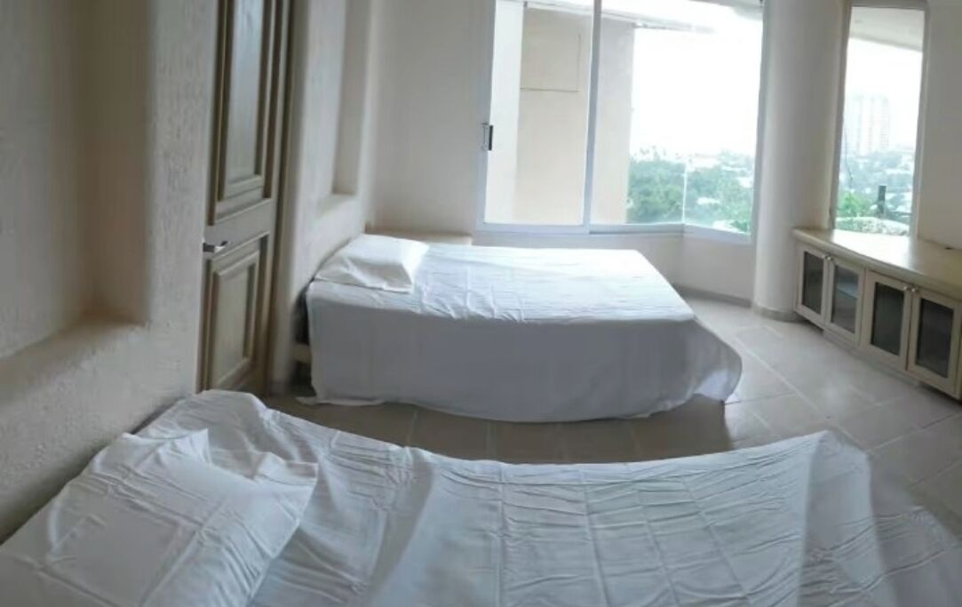 A room with two beds, a large window, and a view of the city.