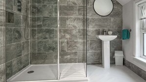 Uma casa de banho moderna com chuveiro em cabine de vidro, lavatório pedestal branco e espelho redondo.