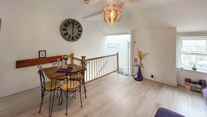 Uma sala de jantar com uma mesa e cadeiras de madeira, um relógio na parede e um lustre.