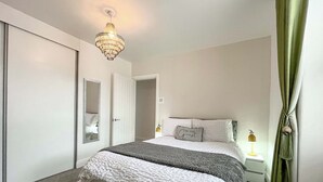 Ein Schlafzimmer mit einem Bett, einer Deckenleuchte, einem Nachttisch, einem Spiegel und einer Tür.
