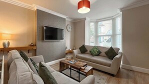 Ein Wohnzimmer mit Flachbildfernseher, einer Couch, einem Couchtisch und einem Fenster mit Jalousien.