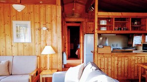 A wooden cabin interior with a sofa, a lamp, a refrigerator, and a kitchen area. - Conifer Chalet 5 - UKC5219 (Crieff)