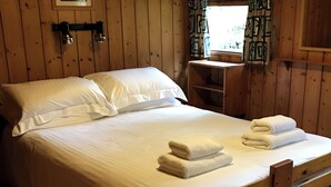 A wooden-paneled room with a bed, a nightstand, a window with curtains, and a shelf. - Conifer Chalet 5 - UKC5219 (Crieff)