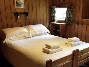 A wooden-paneled room with a bed, a nightstand, a window with curtains, and a shelf. - Conifer Chalet 5 - UKC5219 (Crieff)