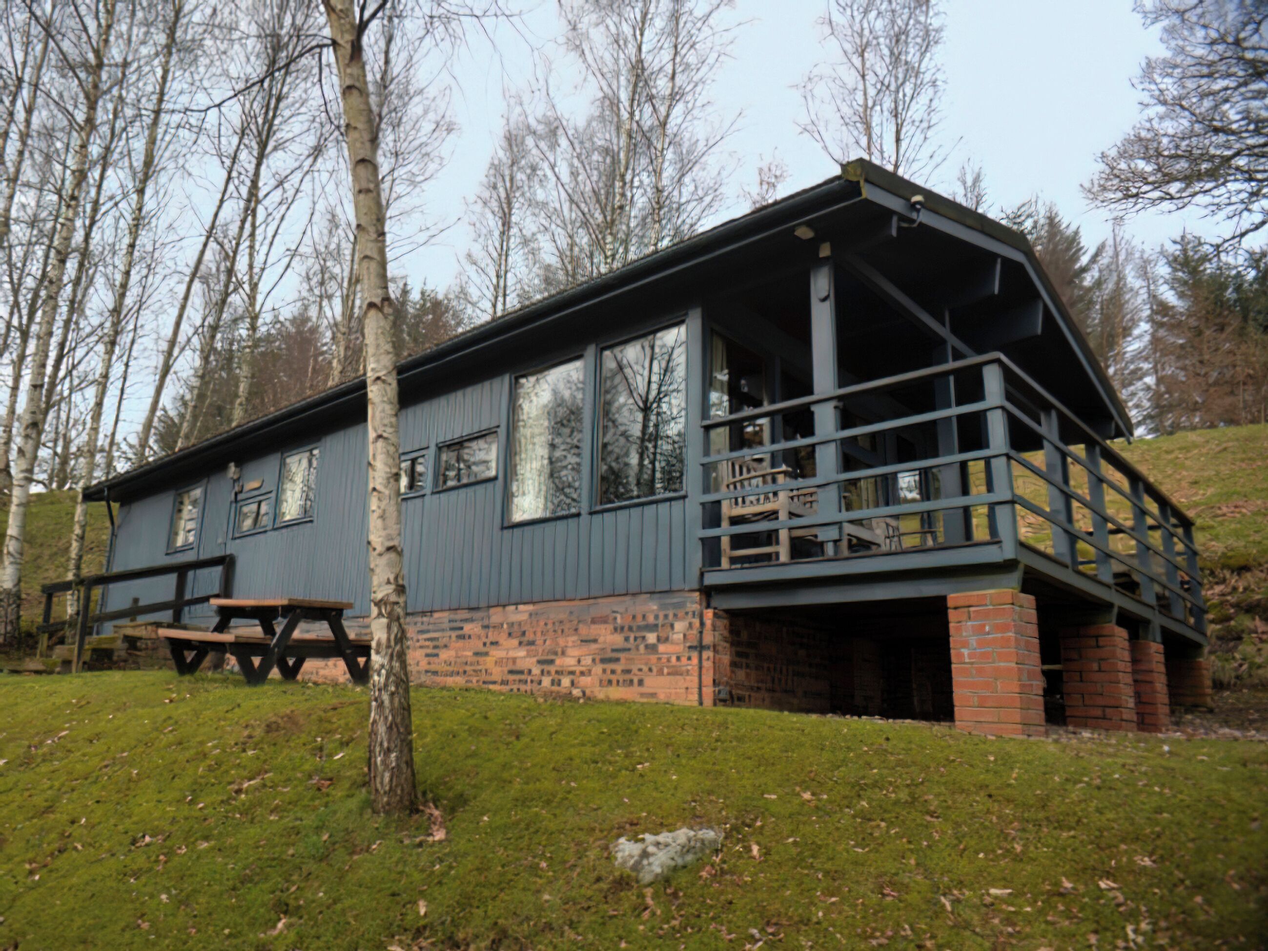 A cabin with a balcony, a picnic table, and a brick foundation.