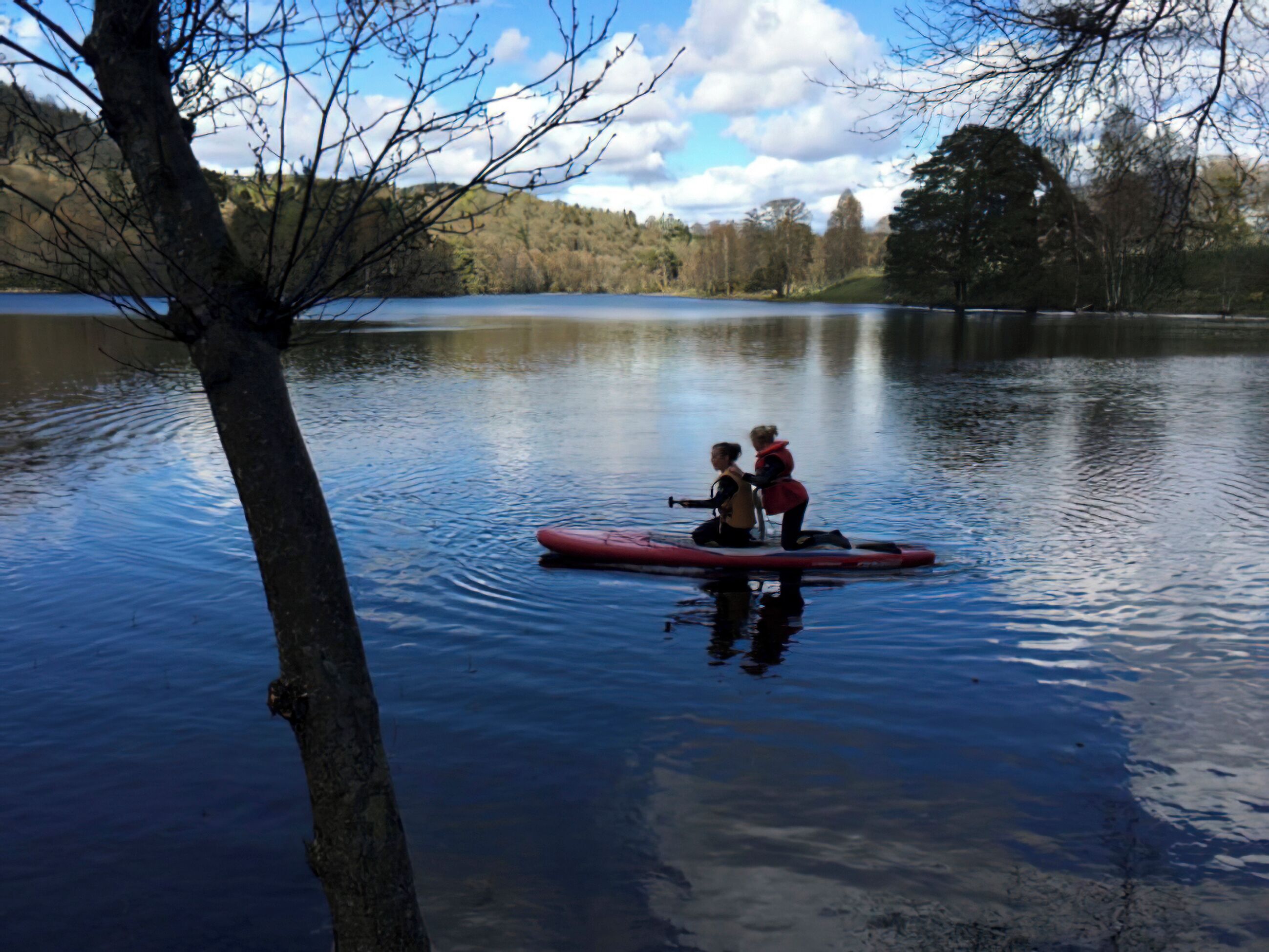 A calm lake with two people on a red paddleboard.