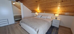 A bedroom with a bed, bedside tables, a nightstand, a lamp, and a wooden ceiling.