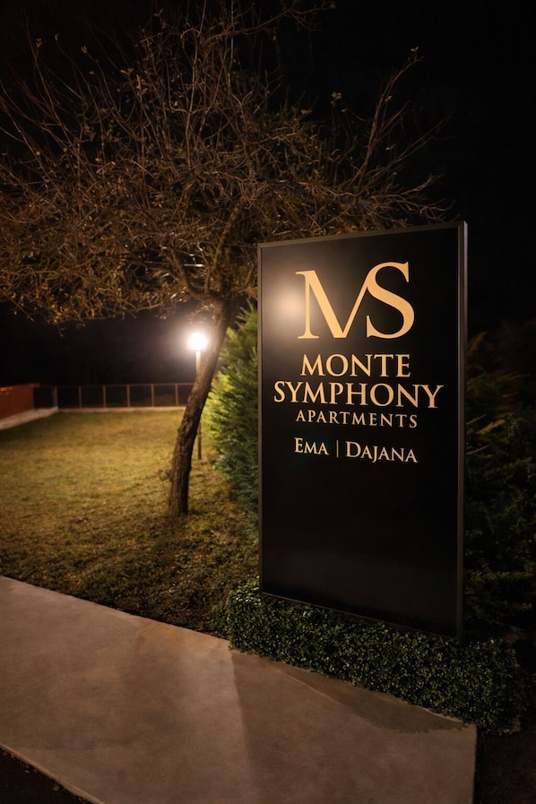Señal de los Apartamentos Monte Symphony, con un árbol y un camino en primer plano.