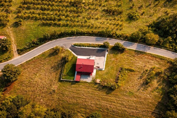 An aerial view of a property with a red-roofed building, surrounded by a landscaped area and a curved road.