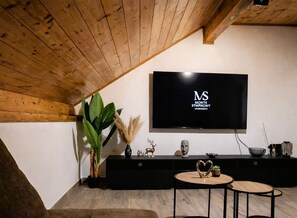 Una sala de estar moderna con techo de madera, mueble de entretenimiento negro, televisor grande y una mesa de centro redonda.